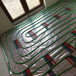 Zielone rury ogrzewania podłogowego ułożone na folii z siatką i logo, widok z góry, przygotowanie do wylewki.