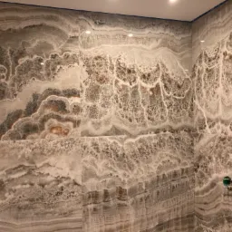 Ściana w łazience wyłożona dużymi płytami z wzorem imitującym marmur onyx w odcieniach szarości, brązu i bieli, widoczny fragment instalacji wodnej.