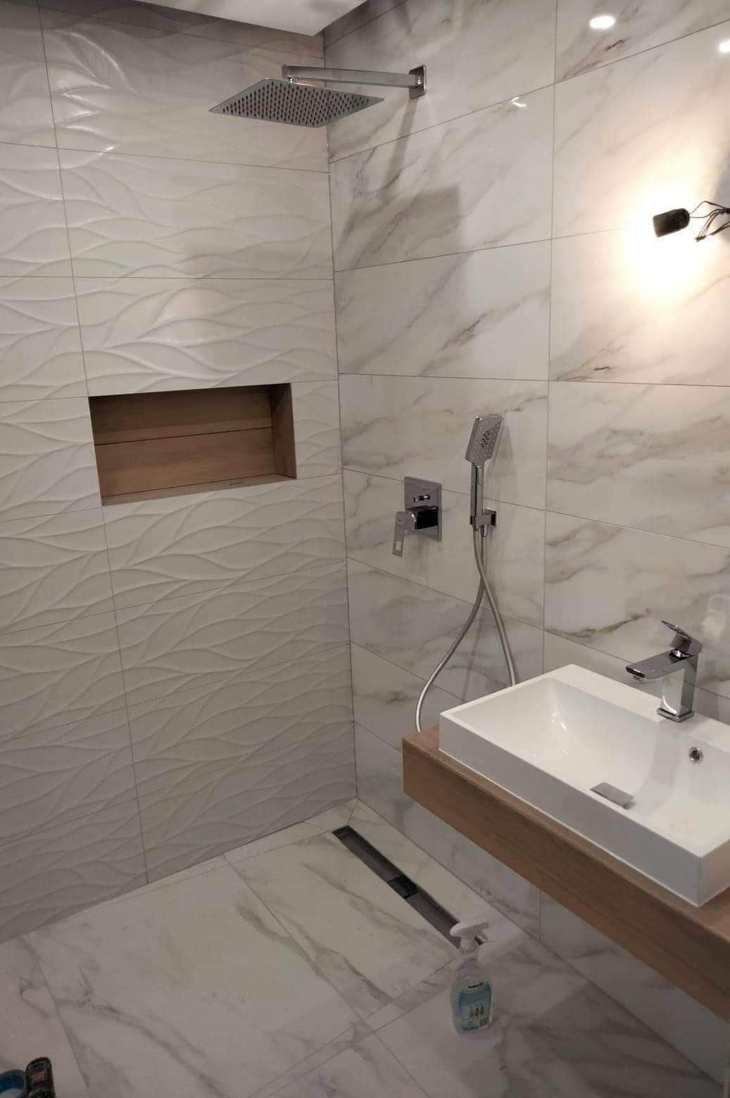 Nowoczesna łazienka z biało-szarymi płytkami imitującymi marmur, deszczownicą, wnęką z drewnianym wykończeniem oraz odpływem liniowym przy ścianie