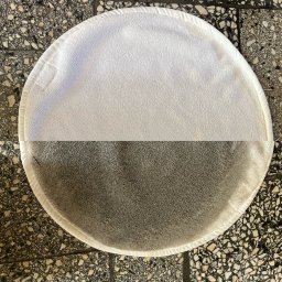 CzystowDomku - Okrągła, biała ścierka do polerowania, widoczna w połowie czysta, w połowie zabrudzona, leżąca na posadzce z lastryko we Wrocławiu.