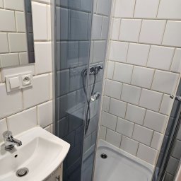 CzystowDomku - Wnętrze łazienki z umywalką i kabiną prysznicową wyłożoną białymi i szarymi płytkami.