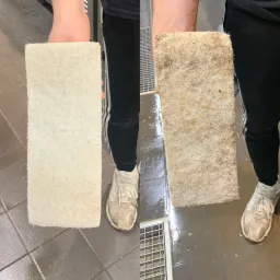 Porównanie czystej i brudnej prostokątnej gąbki do czyszczenia, trzymanej w dłoni, na tle mokrej podłogi z odpływem liniowym