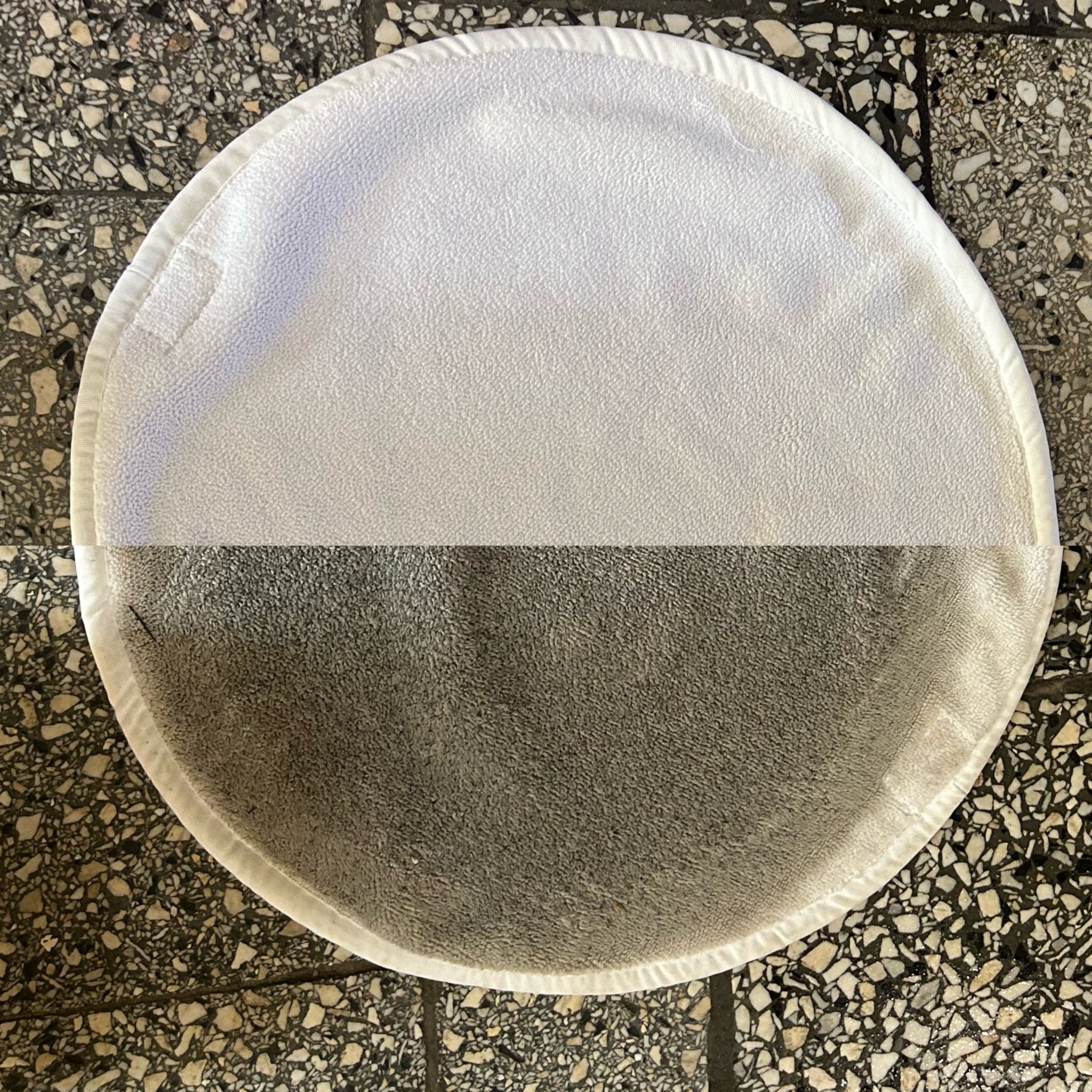 Okrągła, biała ścierka do polerowania, widoczna w połowie czysta, w połowie zabrudzona, leżąca na posadzce z lastryko we Wrocławiu.