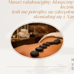 Owalne ujęcie pleców z rozłożonymi, ciepłymi, gładkimi, czarnymi kamieniami, w tle ręczniki i kosmetyki w spa.