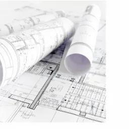 Architektoniczne plany budynku rozłożone na płasko, z kilkoma zrolowanymi kopiami na wierzchu, oświetlone jasnym, neutralnym światłem.