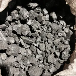 Wnętrze worka wypełnionego bryłami węgla, widoczne nieregularne kształty i struktura materiału, oświetlenie podkreśla krawędzie i fakturę.