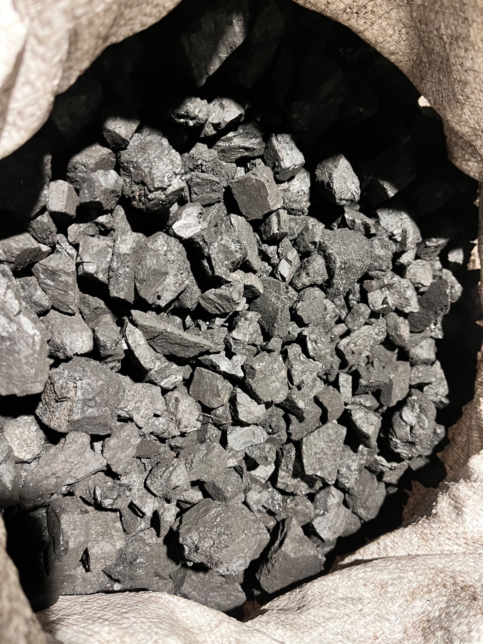 Wnętrze worka wypełnionego bryłami węgla, widoczne nieregularne kształty i struktura materiału, oświetlenie podkreśla krawędzie i fakturę.