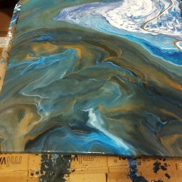 Jag-Woj - Abstrakcyjny obraz na płótnie w odcieniach błękitu, bieli i złota, przypominający wzburzone morze lub marmur, leżący na kartonach z plamami farby.