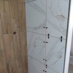 Jag-Woj - Proces układania płytek imitujących drewno i marmur w rogu łazienki z użyciem lasera krzyżowego i przyssawek do płytek.