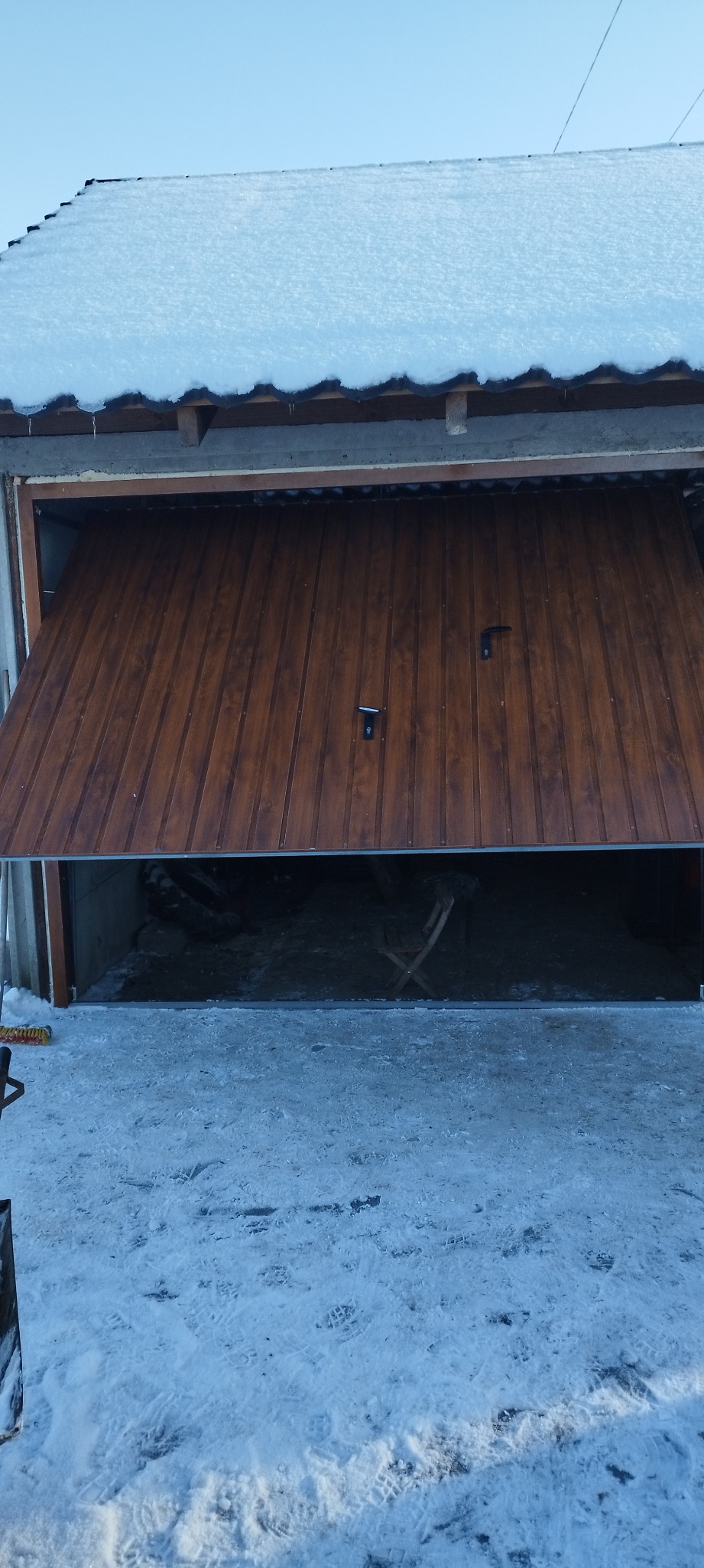 Otwarta, brązowa brama garażowa segmentowa z dwoma uchwytami, widok na wnętrze garażu w zimowy dzień, śnieg na dachu i przed garażem.