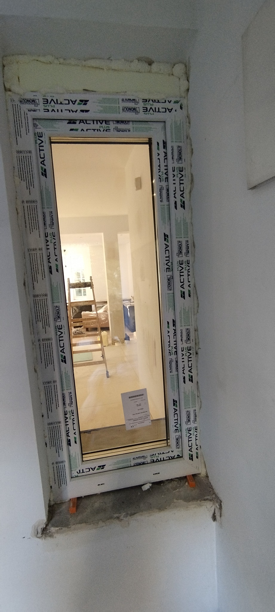 Nowo zamontowane okno PCV z widoczną pianką montażową wokół ramy, w tle widoczny drabina i materiały budowlane.