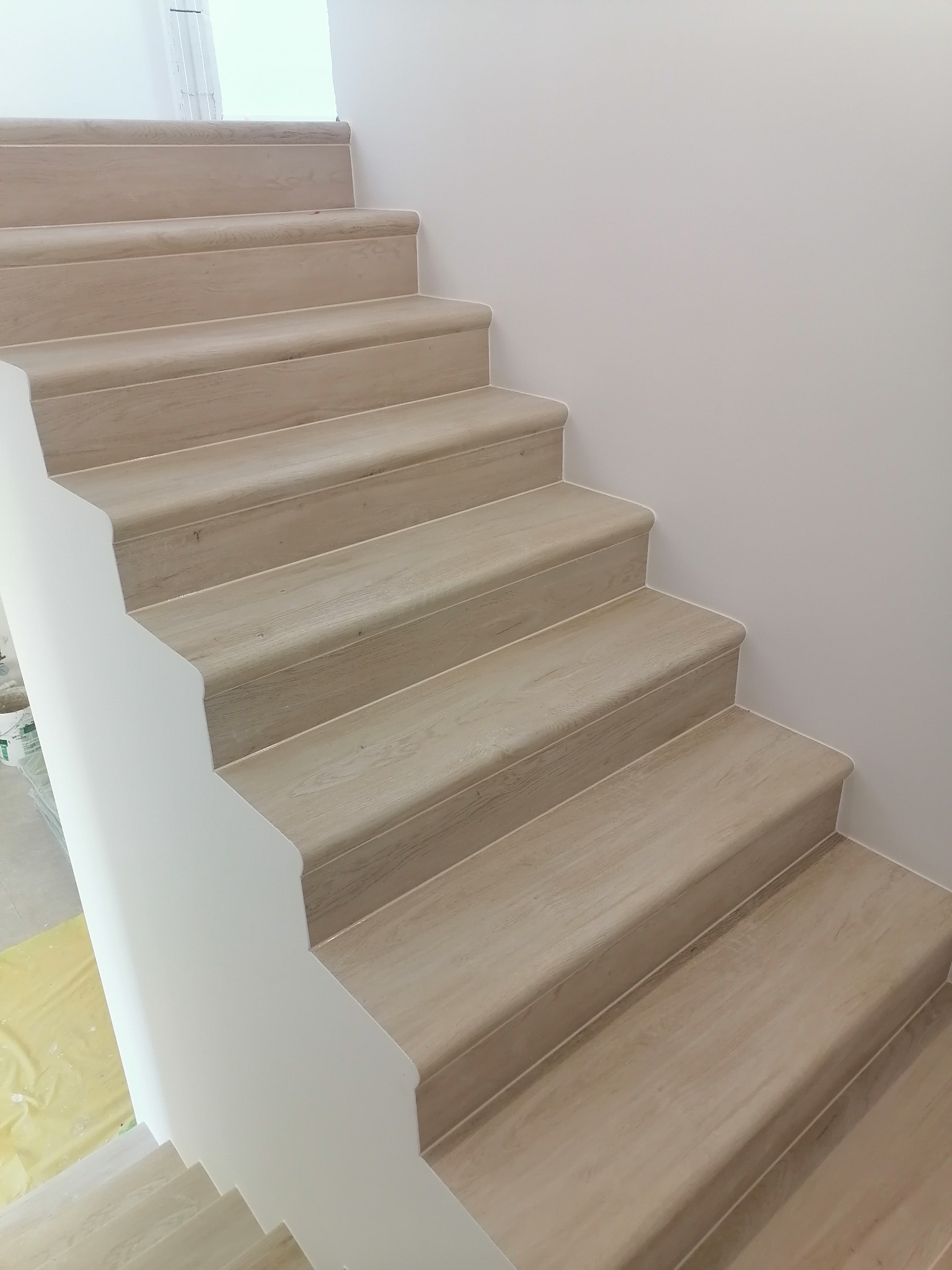 Jasne, drewnopodobne schody z zaokrąglonymi krawędziami w nowym domu w Warszawie, widok z dołu.