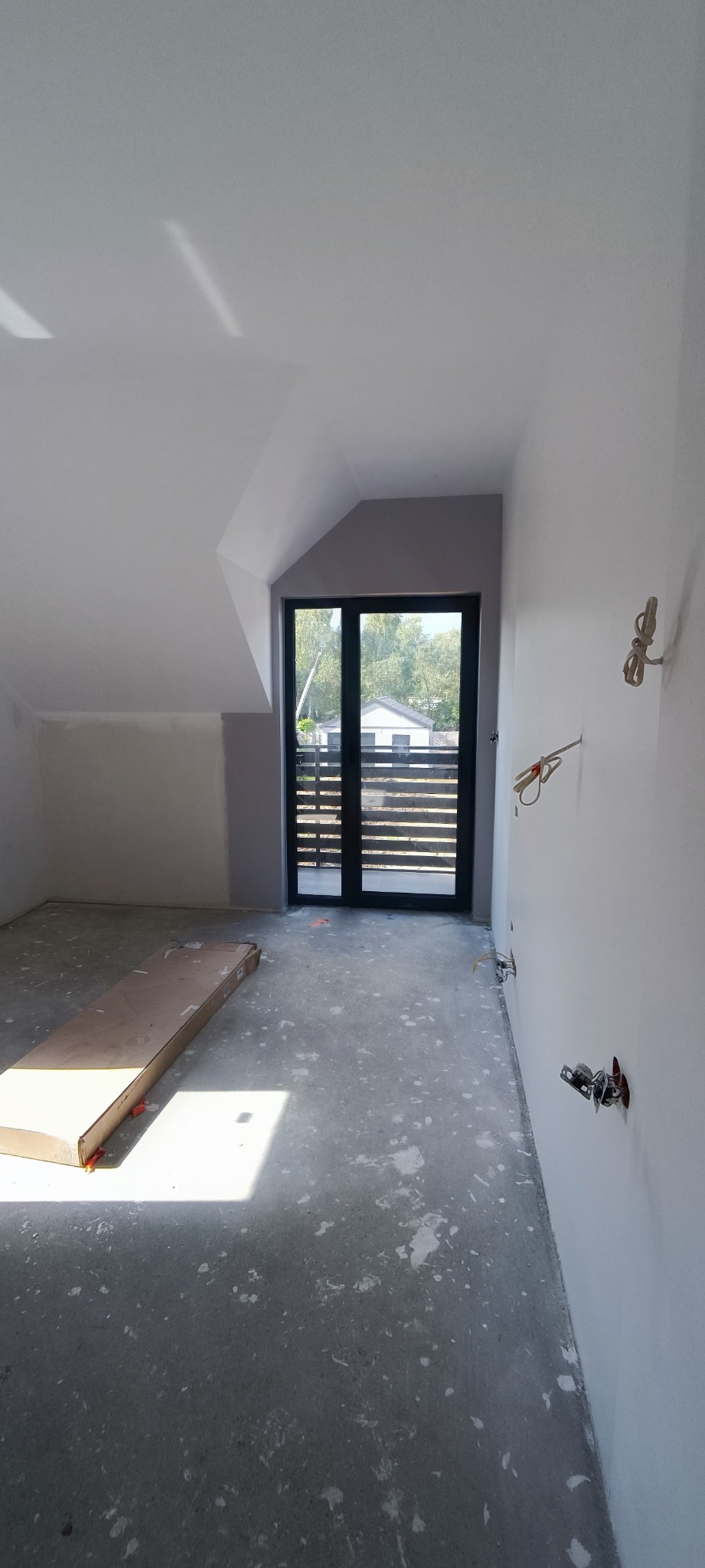 Wnętrze poddasza po szpachlowaniu ścian, z widocznymi puszkami elektrycznymi i kartonem na podłodze, przygotowane do dalszych prac wykończeniowych.