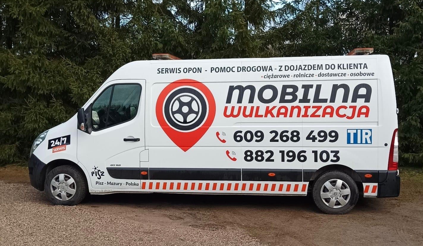 Biały bus serwisu opon z napisem 'Mobilna Wulkanizacja' i numerami telefonów, zaparkowany przed drzewami.