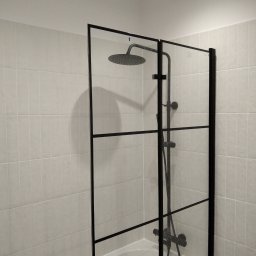 MK Spec - Kabina prysznicowa typu walk-in z czarnymi profilami i deszczownicą zamontowana nad wanną, wykończona jasnymi płytkami ceramicznymi.