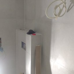 MK Spec - Wnętrze łazienki w trakcie remontu: widoczna zabudowa stelaża WC z płyt karton-gips, przygotowana do położenia płytek, z widocznymi instalacjami hydraulicznymi i elektrycznymi, na górze leżą...