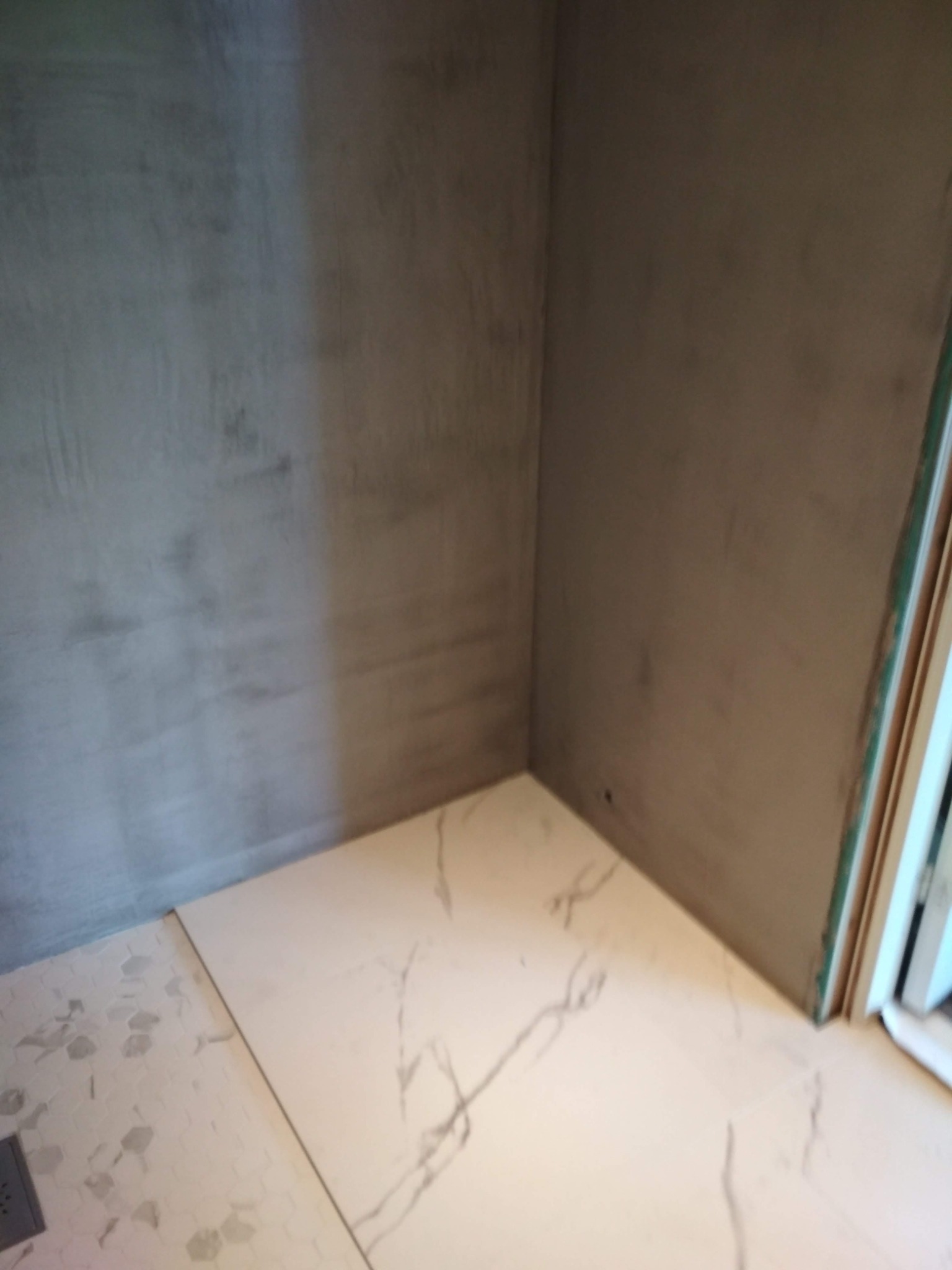 Narożnik łazienki z wyłożonymi płytkami podłogowymi imitującymi marmur i surowymi, szarymi ścianami przygotowanymi pod gładź.