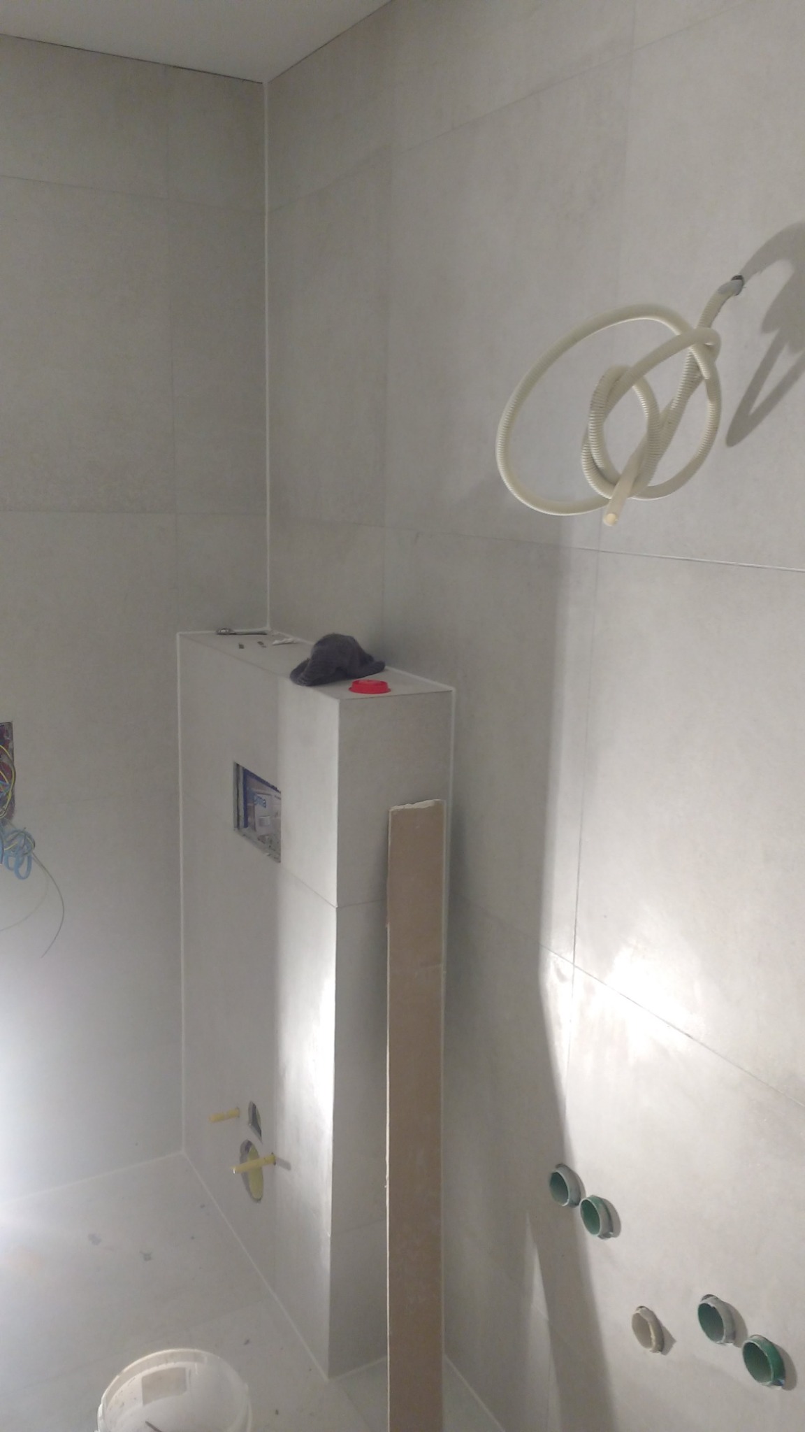 Wnętrze łazienki w trakcie remontu: widoczna zabudowa stelaża WC z płyt karton-gips, przygotowana do położenia płytek, z widocznymi instalacjami hydraulicznymi i elektrycznymi, na górze leżą...