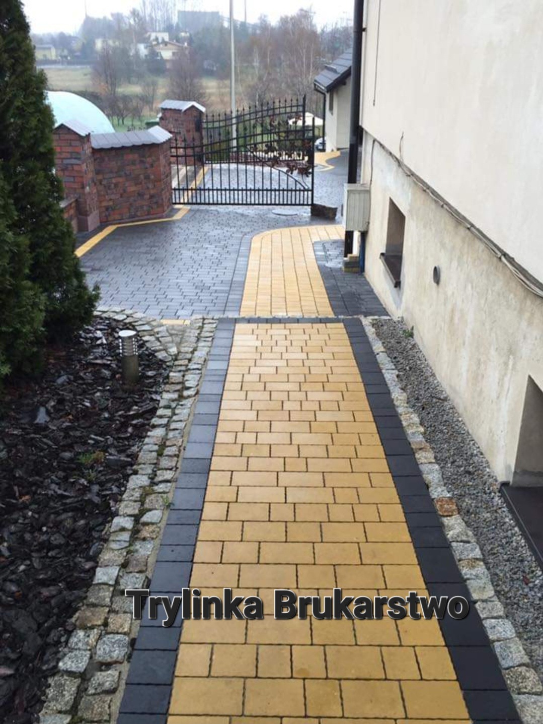 Żółto-czarna ścieżka z kostki brukowej prowadząca od domu do bramy wjazdowej, obrzeża z kostki granitowej, widok z góry, pochmurny dzień.