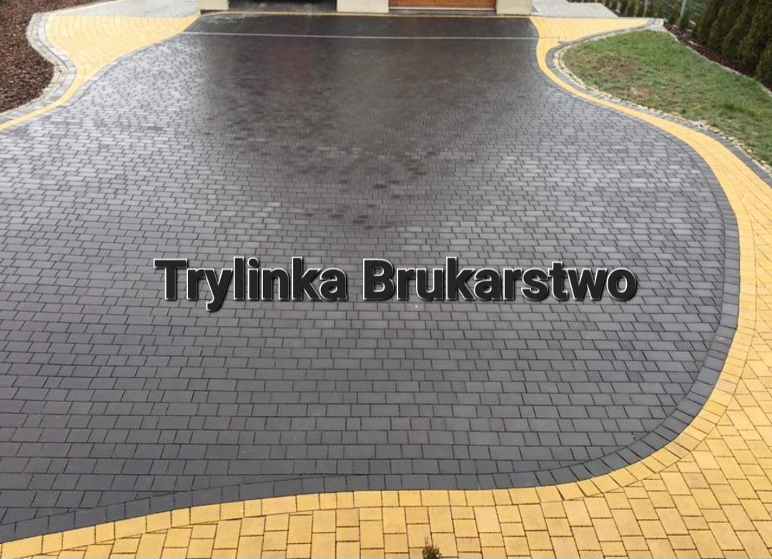 Ułożona, ciemnoszara kostka brukowa z żółtą obwódką prowadząca do garażu, widoczny napis 'Trylinka Brukarstwo'.