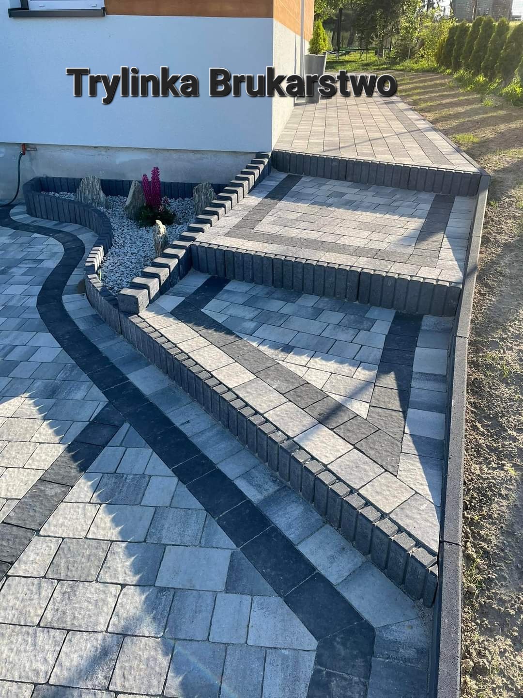 Schody i ścieżka z kostki brukowej w odcieniach szarości i czerni, z elementami dekoracyjnymi w postaci kamieni i roślin, prowadzące do domu.