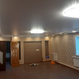 WorkBud - Pokój po remoncie z brązową podłogą, wzorzystą tapetą, białymi grzejnikami, dwoma niedopasowanymi drzwiami i oświetleniem sufitowym.