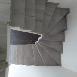 Spiralne schody wyłożone szarymi płytkami ceramicznymi, widok z góry, widoczne niedociągnięcia w wykończeniu na pierwszym stopniu.