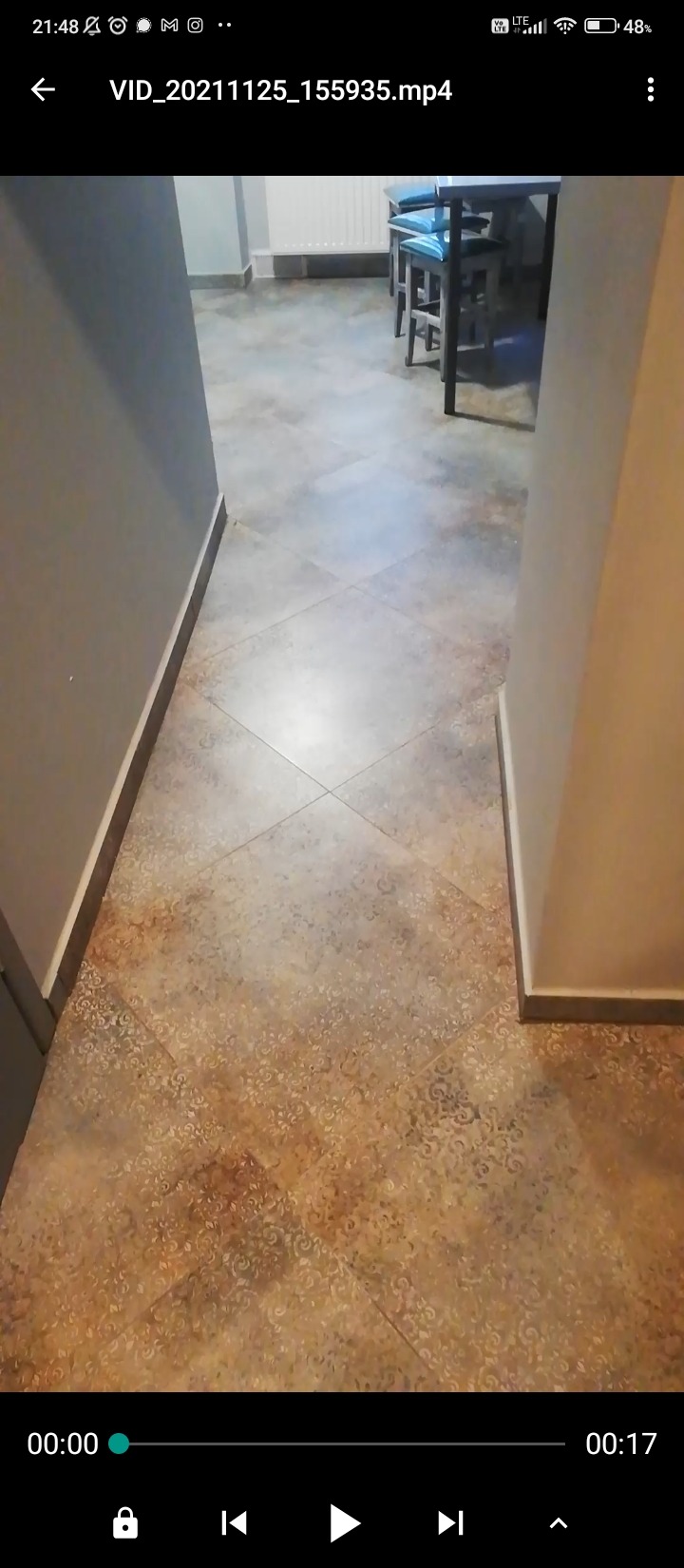 Ułożona pod kątem brązowo-beżowa podłoga z płytek ceramicznych we wzory, widok z perspektywy wejścia do pomieszczenia, w tle fragment stołu i krzeseł.