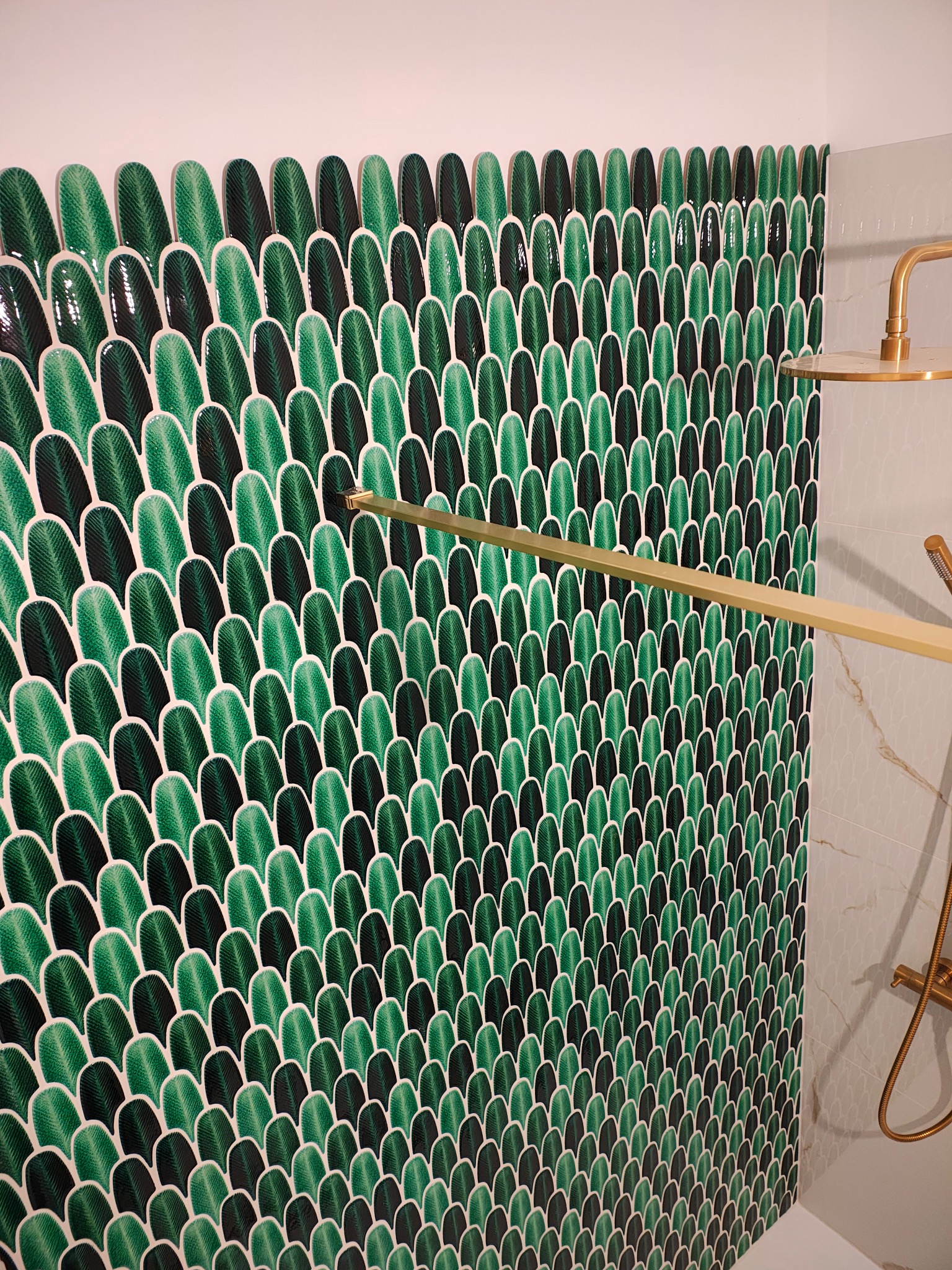 Ściana w łazience wykończona dekoracyjnymi, zielono-czarnymi płytkami w kształcie liści, z elementami złotej armatury prysznicowej. Nowoczesny design.