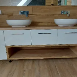 Łazienka w skandynawskim stylu: białe szafki z drewnianym blatem i umywalkami nablatowymi, drewniana okładzina ściany, widoczne ukośne sufity.