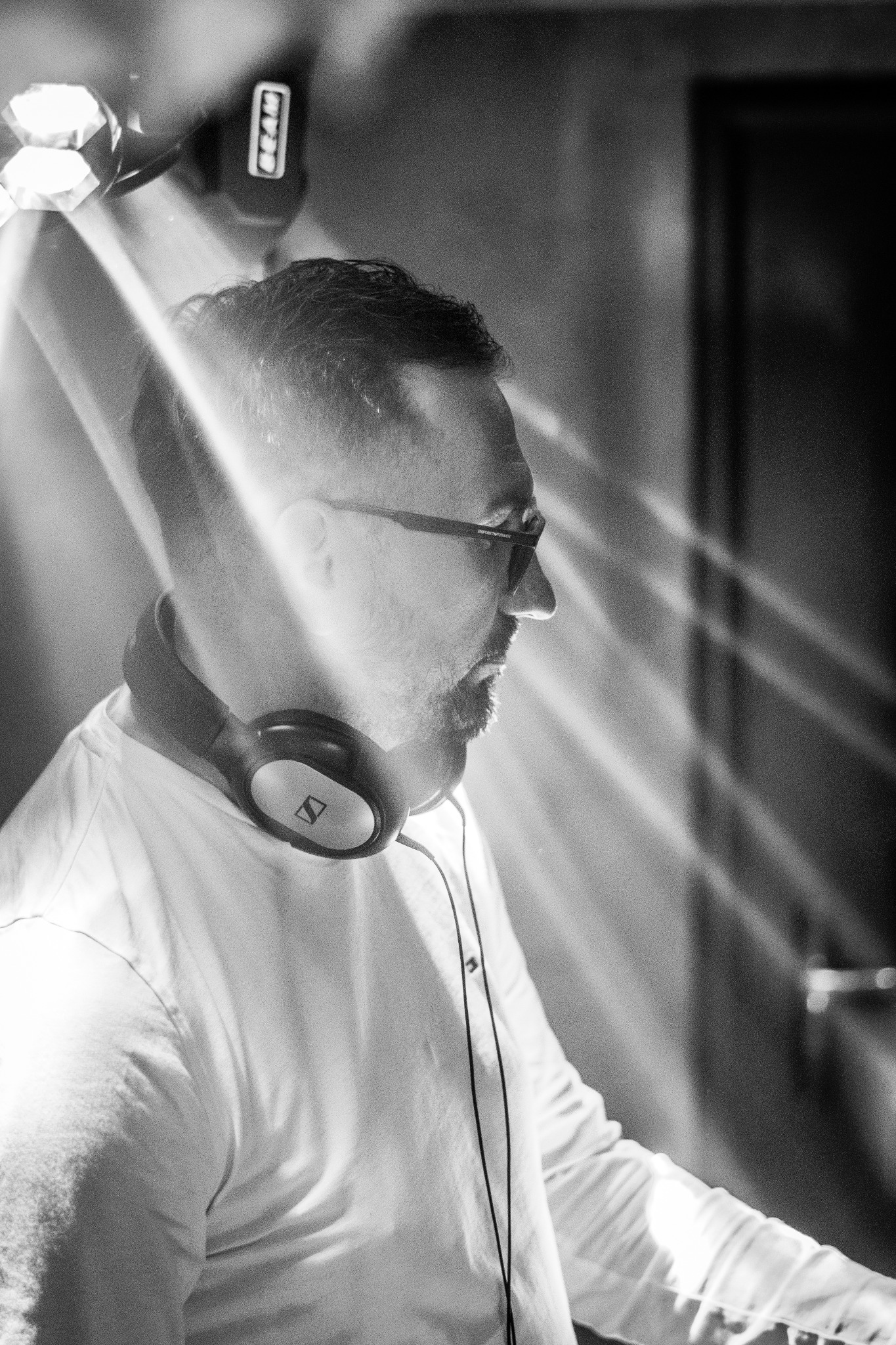 Profil mężczyzny w okularach i słuchawkach Sennheiser, oświetlonego promieniami światła z reflektora Beam, w czarno-białej stylistyce.