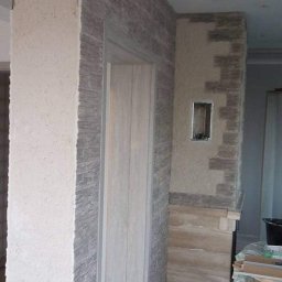 ROMBUD - Fragment ściany z dekoracyjnym tynkiem i kamieniem, widoczny również otwór na gniazdko elektryczne w trakcie przygotowania.