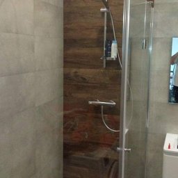 ROMBUD - Nowoczesna kabina prysznicowa z panelami imitującymi drewno i szarymi płytkami, widok z boku, chromowana armatura.