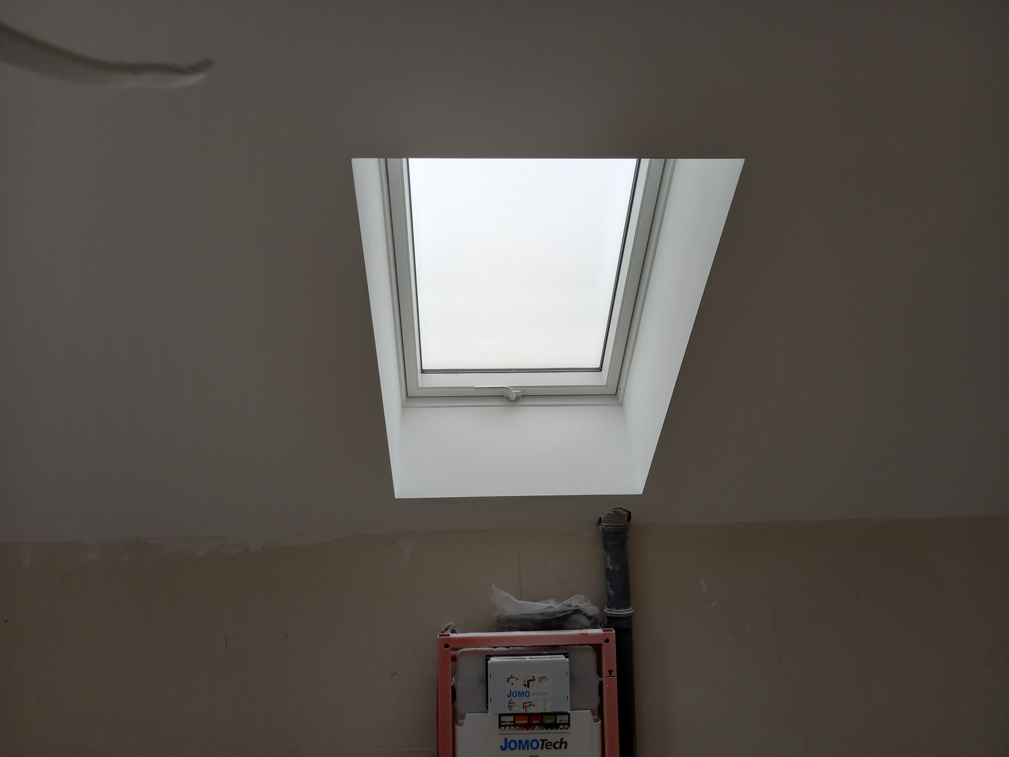 Montaż stelaża podtynkowego WC JomoTech pod oknem dachowym w trakcie prac wykończeniowych łazienki, widoczne ślady po szpachlowaniu na ścianie.