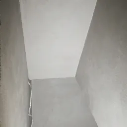 Wnętrze w Grodzisku Wielkopolskim po nałożeniu szarej warstwy wykończeniowej na ścianach i suficie, widoczne niedoskonałości w narożniku i przy podłodze.