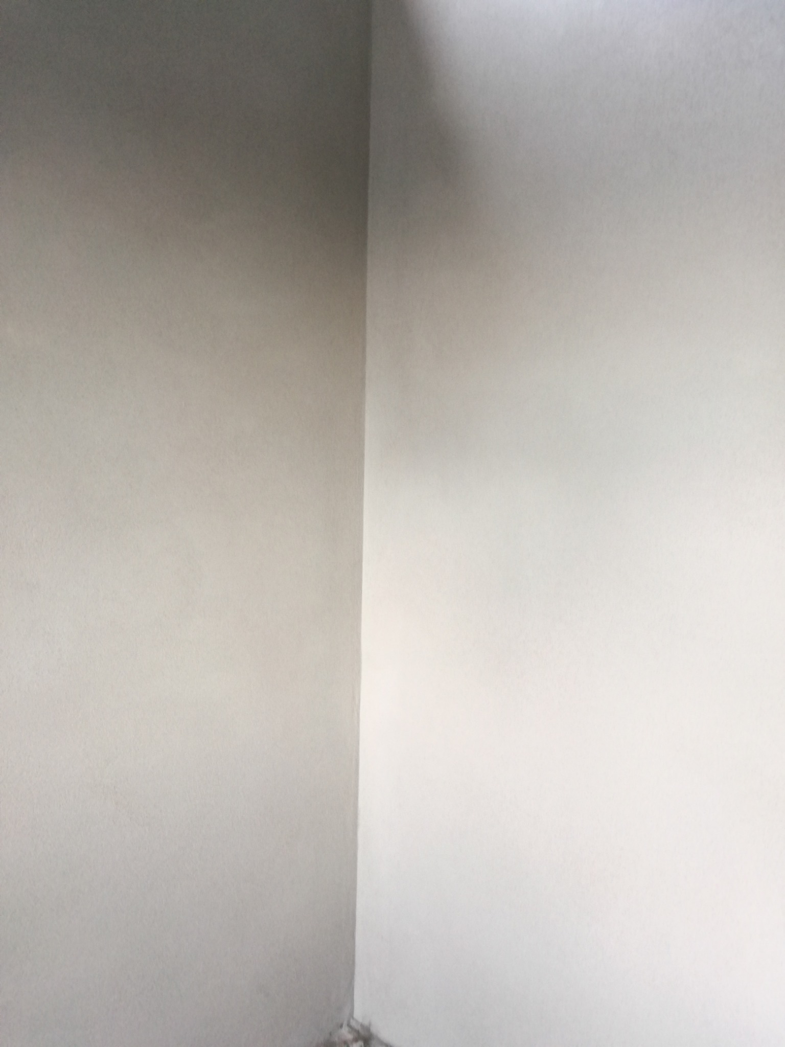 Wewnętrzny narożnik pomieszczenia po nałożeniu jasnoszarej warstwy wykończeniowej, widoczne delikatne różnice w odcieniach na ścianach.