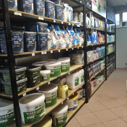 Półki w sklepie budowlanym wypełnione różnorodnymi materiałami wykończeniowymi marki Greinplast, w tym fugi elastyczne, hydroizolacje w płynie, masy szpachlowe i farby fasadowe, ułożone rzędami...