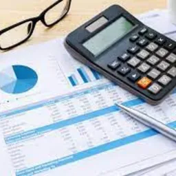 Kalkulator, długopis i kubek na tle dokumentów z danymi finansowymi i wykresem kołowym.