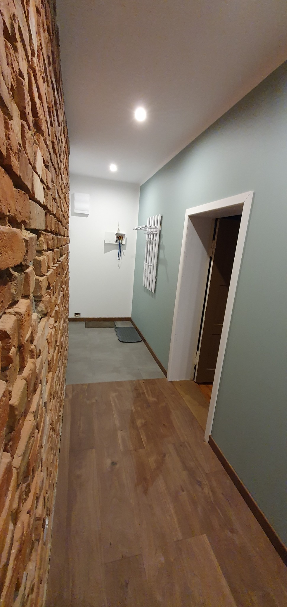Wnętrze korytarza z parkietem, ścianą z cegły i pomalowaną na szaro-zielono ścianą z białymi drzwiami w głębi.