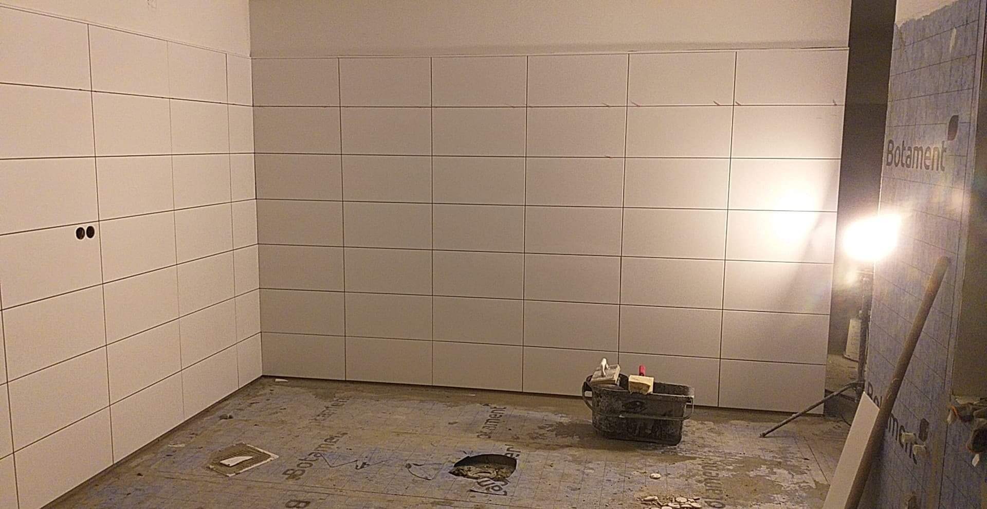 Świeżo wykafelkowana, jasna łazienka z widocznymi narzędziami glazurniczymi i materiałami budowlanymi na podłodze.