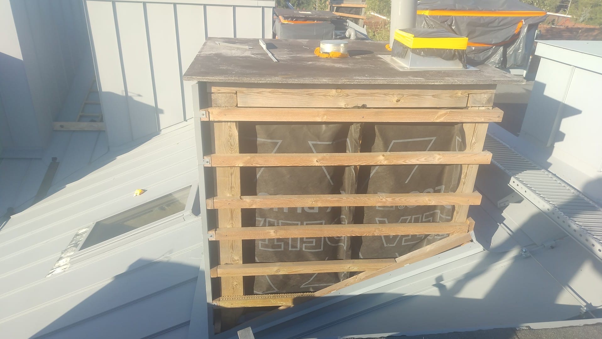 Szary dach z blachy trapezowej i drewniana konstrukcja komina w Łagiewnikach. Widoczne okno dachowe i elementy obróbki blacharskiej.