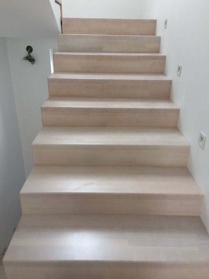 Jasne, drewniane schody wewnętrzne z minimalistycznym oświetleniem punktowym w ścianie, widok z dołu na górę.