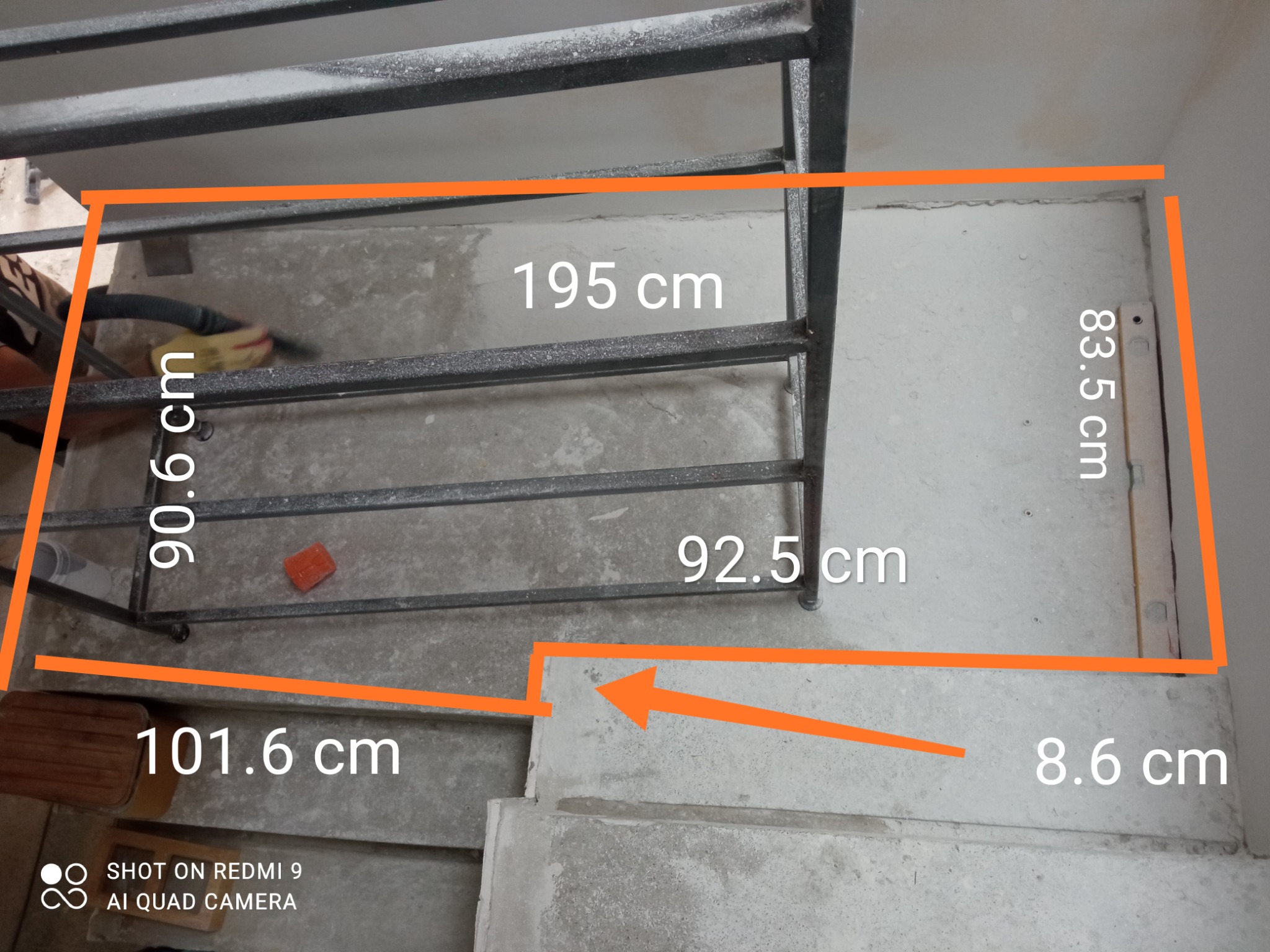 Pomiar powierzchni pod przyszłą antresolę z metalową konstrukcją, widoczne wymiary naniesione na zdjęcie, betonowa podłoga w trakcie sprzątania odkurzaczem.