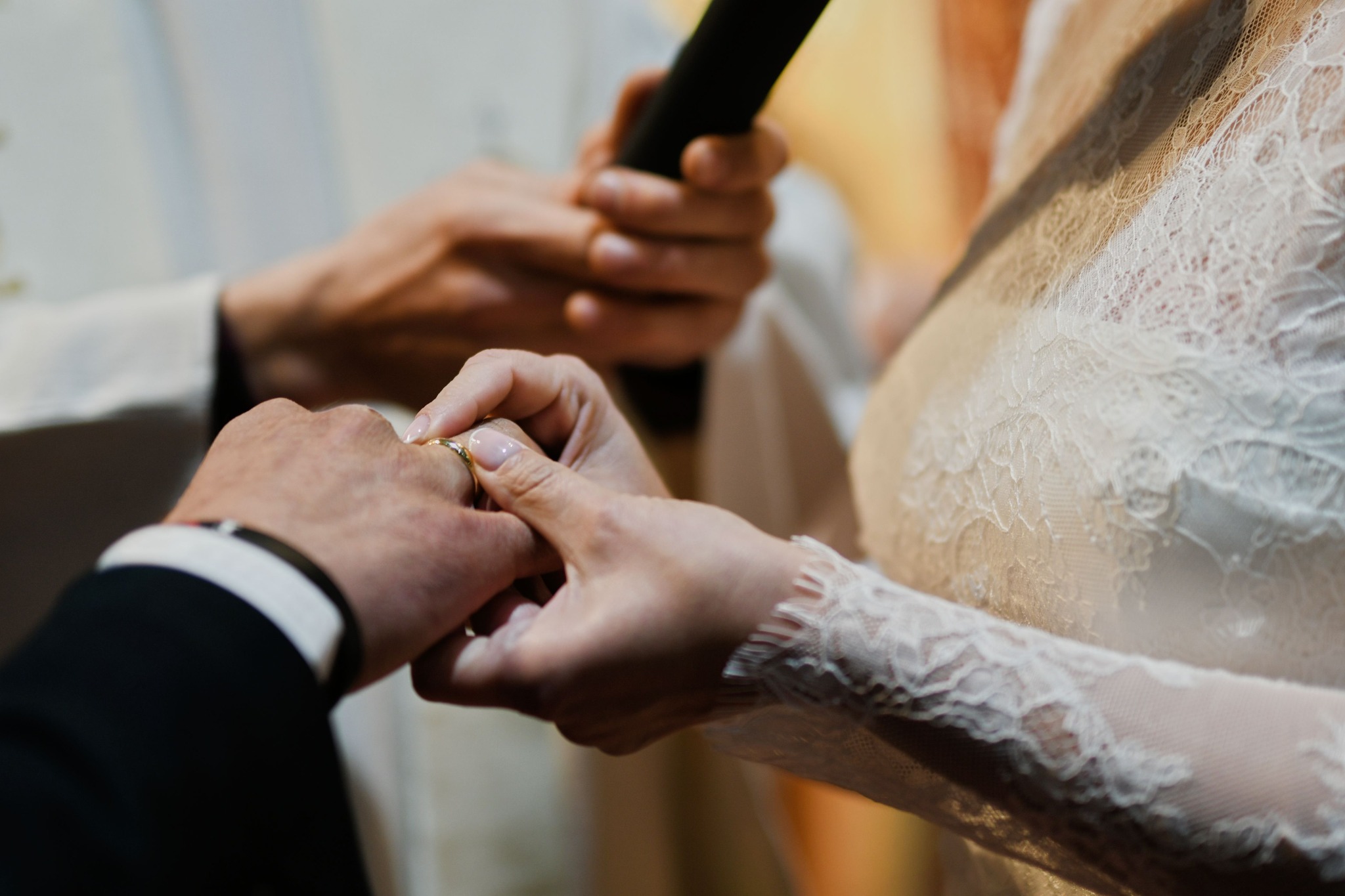 Panna młoda zakłada obrączkę na palec pana młodego podczas ceremonii ślubnej, mikrofon w tle.