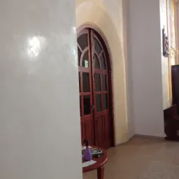 Ściana z efektem dekoracyjnym, widoczna obok drewnianych drzwi w łukowatym przejściu, z małym stolikiem i butelką z rozpylaczem w tle.