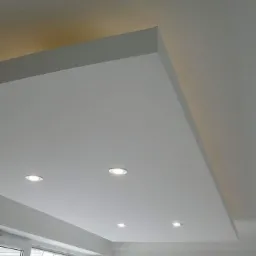 Biały sufit podwieszany z płyt kartonowo-gipsowych z wbudowanymi punktowymi lampami LED, widoczne okno z białymi ramami.