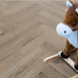 Jasna podłoga ułożona w jodełkę z drewnianym konikiem na biegunach w prawym rogu.