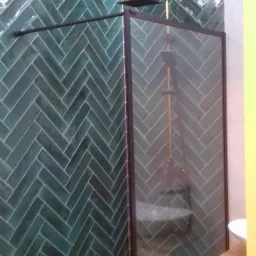 Kabina prysznicowa z zielonymi płytkami ułożonymi w jodełkę, oświetleniem LED i czarną ramą w łazience w Sosnowcu.