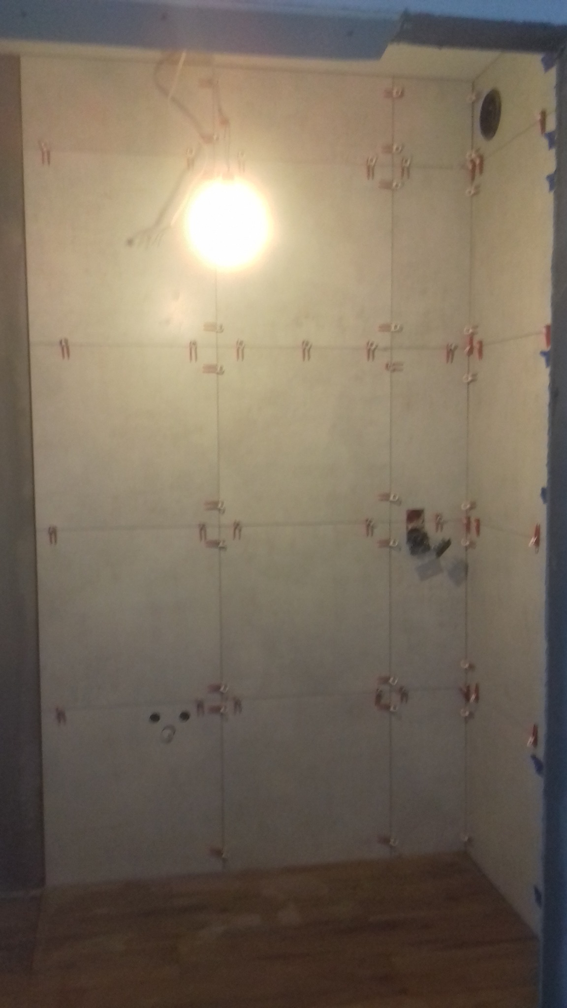 Ściany w trakcie układania płytek ceramicznych, widoczne krzyżyki dystansowe, instalacja elektryczna w ścianie, oświetlenie halogenowe w górnej części.