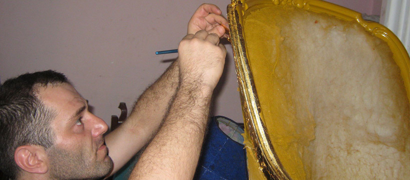 Renowacja ramy lustra: mężczyzna precyzyjnie nakłada płatki złota na żółtą ramę lustra, używając cienkiego pędzla.